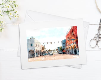 May include: A watercolor painting of a street scene in Venice, California. The street is lined with colorful buildings and palm trees. The sign "VENICE" is visible in the center of the image.