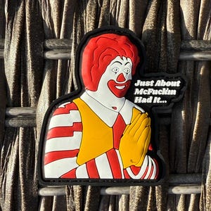 K&ouml;nnte beinhalten: Ein gestickter Aufn&auml;her mit einem Comic-Charakter mit einer roten Per&uuml;cke und einem gelb-rot gestreiften Hemd. Der Charakter h&auml;lt seine H&auml;nde zum Beten zusammen. Der Text "Just About McFuckin Had It..." ist in Wei&szlig; auf schwarzem Hintergrund geschrieben.