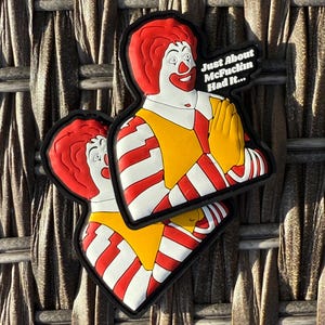 K&ouml;nnte beinhalten: Zwei rot-wei&szlig; gestreifte Patches mit einem Cartoon-Bild von Ronald McDonald. Der obere Patch hat den Text "Just About McFuckin Had It..." Die Patches befinden sich auf einem braunen gewebten Hintergrund.