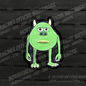 May include: Green monster character with one eye and a toothy grin. The character is standing with its arms at its sides. The background is black with a grid pattern.