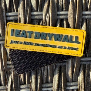 Op de afbeelding: Gele patch met zwarte tekst die "I EAT DRYWALL just a little sometimes as a treat" luidt.