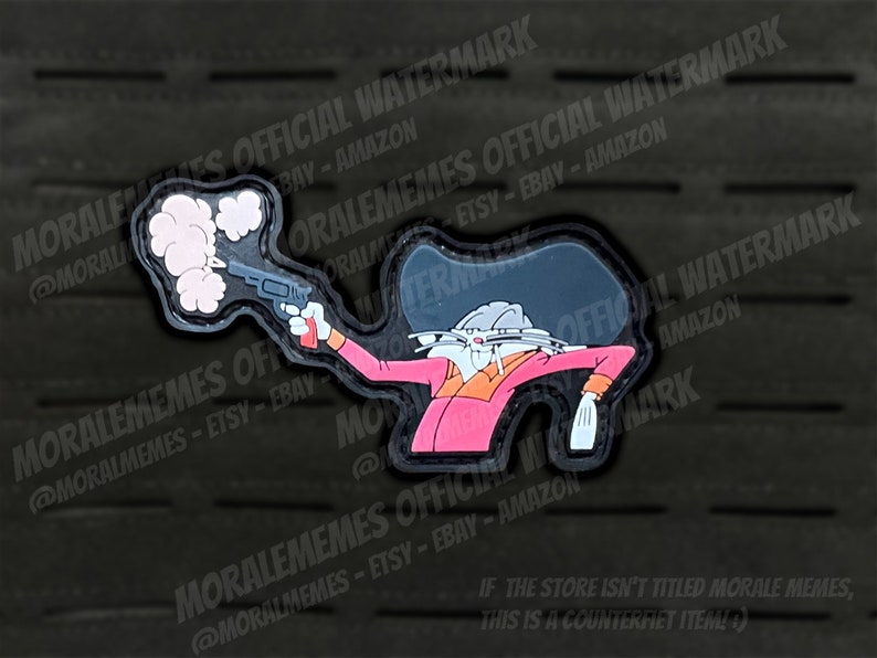 May include: A black and white cartoon character wearing a pink shirt and a black hat, holding a gun with smoke coming out of the barrel. The character is in a shooting pose. The image is a patch.