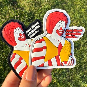 K&ouml;nnte beinhalten: Zwei wei&szlig;-rot gestreifte Patches mit einem Cartoon-Bild von Ronald McDonald. Die Patches haben schwarze R&auml;nder und den Text "Just About McFuckin Had It..." aufgedruckt.