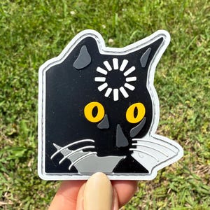 Può includere: Toppa a forma di gatto nero con occhi gialli e un disegno a forma di sole bianco sulla fronte. La toppa ha un bordo bianco e dettagli grigi. Il volto del gatto è un design stilizzato, ideale per abbigliamento o accessori.