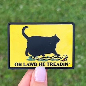 May include: A rectangular patch with a yellow background and a black border. The patch features a black cat silhouette above a yellow snake, with the phrase "OH LAWD HE TREADIN'" in black text.
