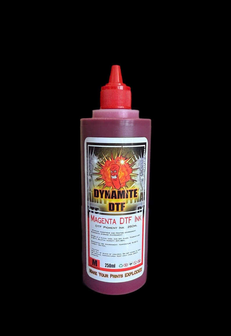 Op de afbeelding: Een fles van 250ml magenta DTF-inkt met een rode draaidop. Het etiket bevat een cartoonfiguur van een dynamietstaaf, de tekst DYNAMITE DTF, MAGENTA DTF INK, 250ML, de slogan MAKE YOUR PRINTS EXPLODE en technische opslaginstructies.