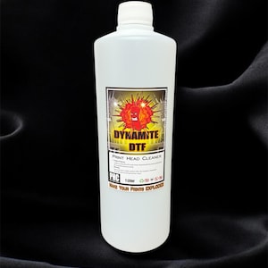 May include: A white plastic bottle with a white cap, labeled "DYNAMITE DTF PRINT HEAD CLEANER." The label features a cartoon explosion graphic. The bottle contains 1 liter of cleaning solution, designed to make prints explode.
