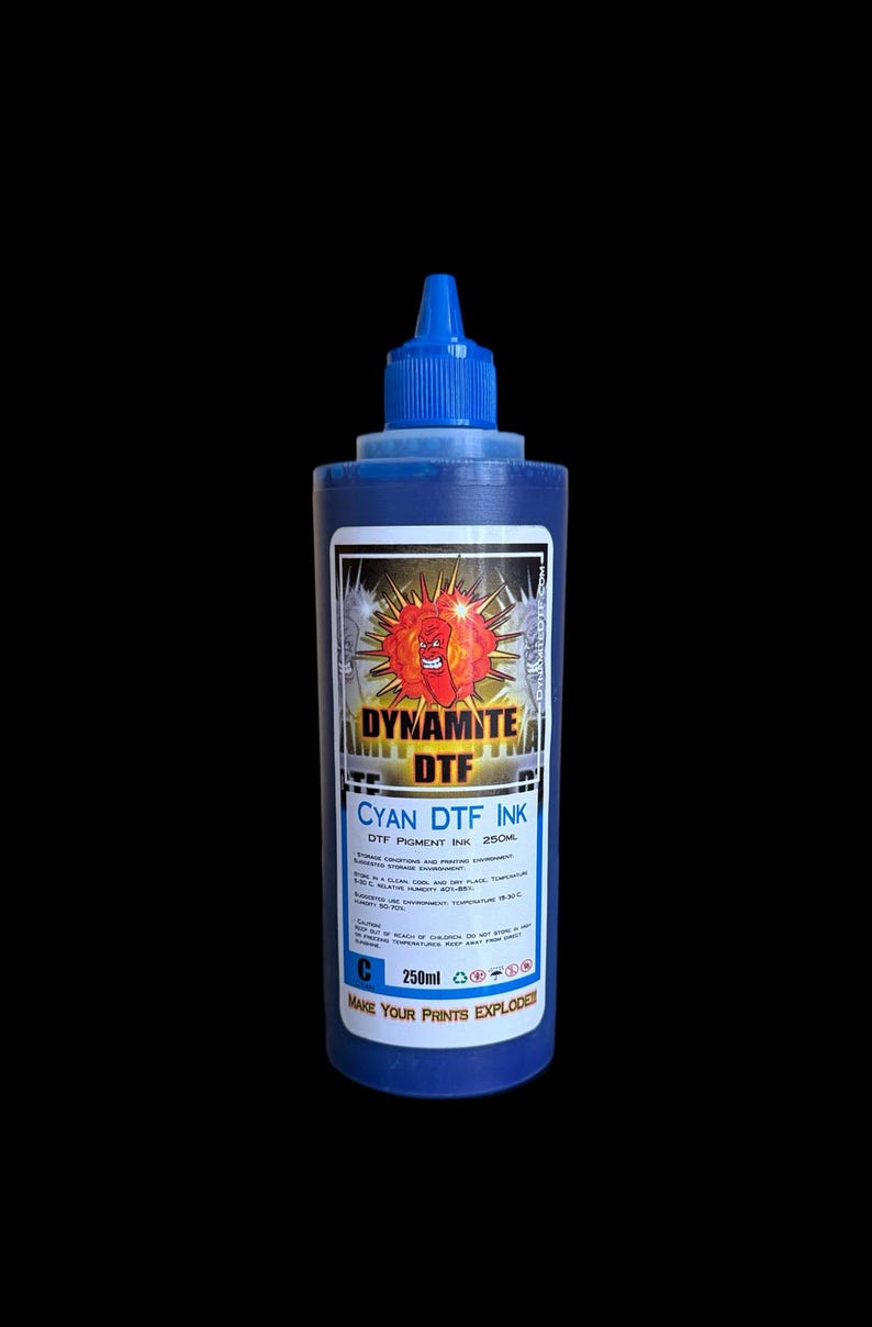 Op de afbeelding: Een blauwe plastic knijpfles met 250ml cyaan DTF-inkt. Het etiket bevat een afbeelding van een rode cartoon-dynamietstaaf, de tekst DYNAMITE DTF, CYAN DTF INK, de slogan MAKE YOUR PRINTS EXPLODE en diverse instructies voor opslag.