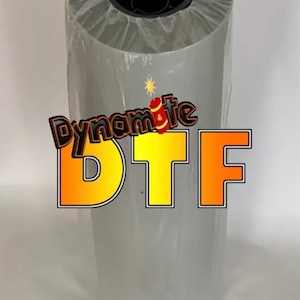 May include: A roll of gray DTF transfer film, wrapped in clear plastic. The text "Dynamite DTF" is displayed in orange and yellow with a firework graphic.