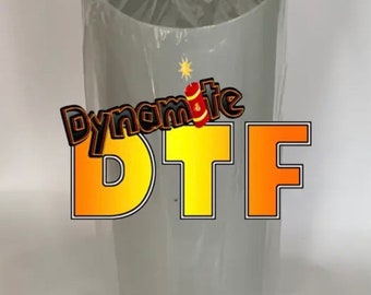 May include: A roll of gray DTF transfer film, wrapped in clear plastic. The text "Dynamite DTF" is displayed in orange and yellow with a firework graphic.