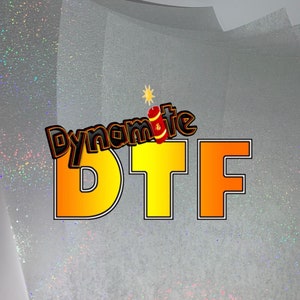 May include: A sheet of white iridescent glitter paper with the text "Dynamite DTF" in yellow and orange letters.