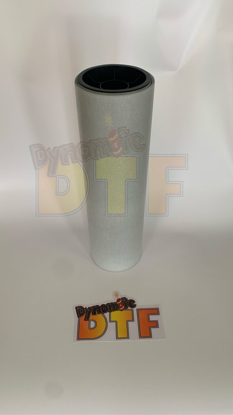 May include: A roll of silver glitter heat transfer vinyl with the text "Dynamite DTF" printed on the roll.