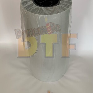 May include: A roll of white vinyl with a clear plastic wrap. The vinyl has the text "Dynamite DTF" printed on it in yellow and orange letters.