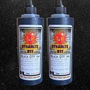 May include: Two black ink bottles with labels reading "DYNAMITE DTF BLACK DTF INK" and a fiery graphic. Each bottle holds 250ml of ink. The text "MAKE YOUR PRINTS EXPLODE" is printed on the bottom of each bottle.