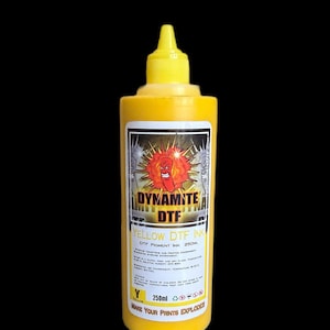 Op de afbeelding: Een gele plastic knijpfles met 250ml Dynamite DTF gele pigmentinkt. Het etiket bevat een cartoonfiguur van een dynamietstaaf, de tekst DYNAMITE DTF, de slogan MAKE YOUR PRINTS EXPLODE en instructies voor opslag en gebruik.