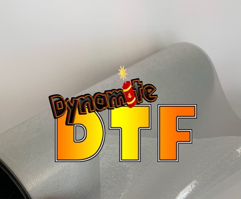 May include: A white, glitter-covered tumbler with the words "Dynamite DTF" in yellow and orange letters. The word "Dynamite" has a red and yellow firework graphic next to it.