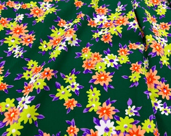 May include: Green fabric with a floral print featuring white, orange, yellow, and purple flowers.