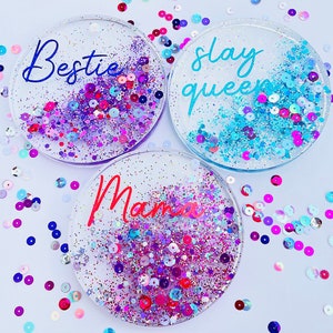 May include: Three round clear resin coasters with glitter and colorful sequins. The coasters have the words "Bestie", "Slay Queen", and "Mama" written on them.