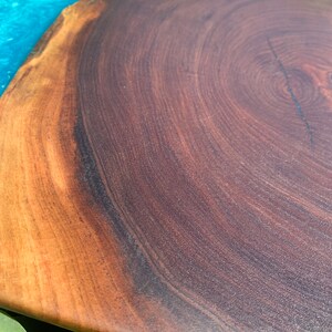 May include: A large, round wooden cutting board with a natural wood grain finish. The board has a blue epoxy resin inlay on one side. The board is perfect for serving cheese, charcuterie, or other appetizers.
