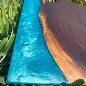 May include: A large wooden cutting board with a blue epoxy resin inlay. The resin has a swirling pattern and a glittery finish. The board has a handle on one end.