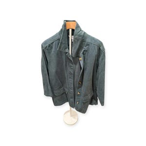 May include: A dark teal corduroy jacket featuring a wide collar, long sleeves, and a front button closure. The jacket includes two large patch pockets at the waist and is displayed on a hanger. The fabric has a visible ribbed texture throughout.