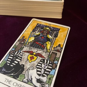May include: The Chariot tarot card features a colorful illustration of a charioteer in armor, driving a chariot pulled by two sphinxes. The card is set against a backdrop of a starry night sky and a cityscape. The card number VII is displayed in the top right corner.