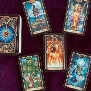 Peut inclure: Cartes de tarot dispos&eacute;es sur une surface en velours violet. Les cartes sont du jeu 'Mystic Mondays' et comprennent le Huit de Coupes, le Jugement, le Diable, le Sept de Pentacles et l'&Eacute;toile.