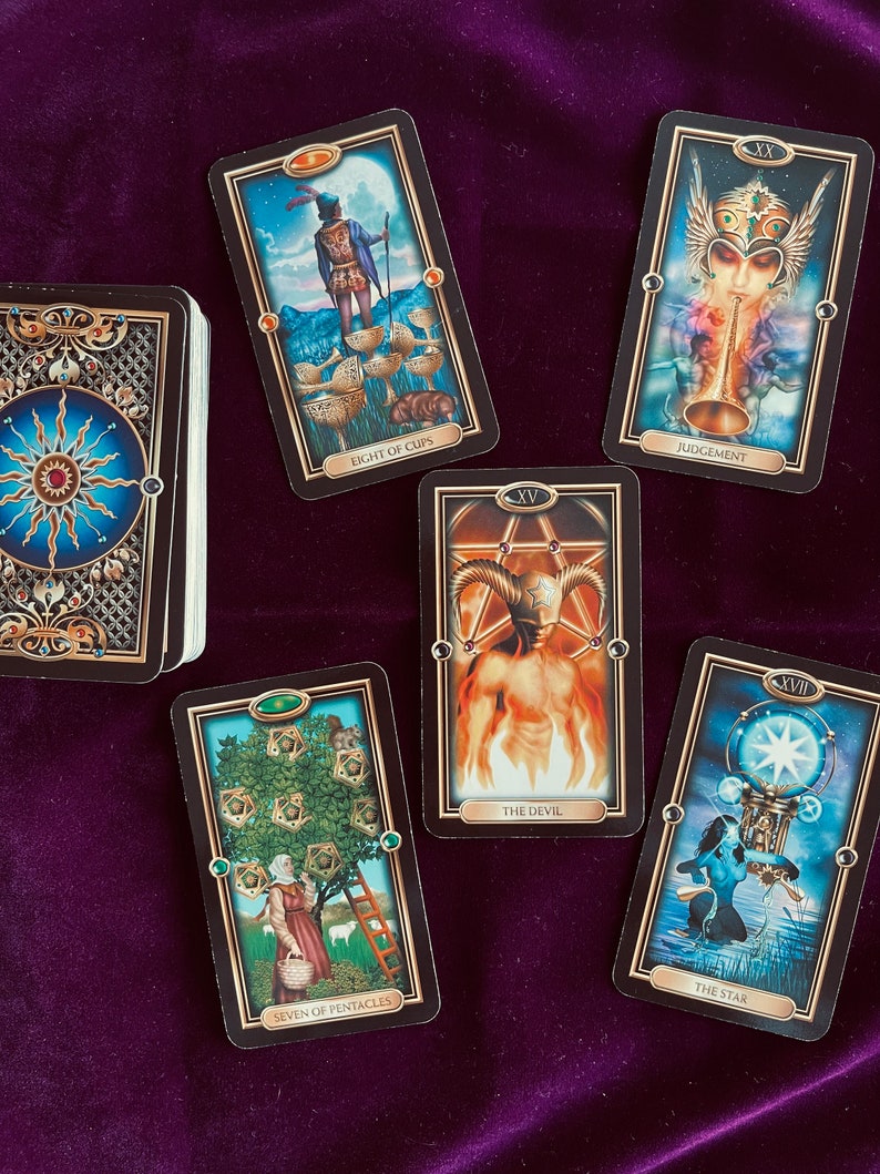 Peut inclure: Cartes de tarot dispos&eacute;es sur une surface en velours violet. Les cartes sont du jeu 'Mystic Mondays' et comprennent le Huit de Coupes, le Jugement, le Diable, le Sept de Pentacles et l'&Eacute;toile.