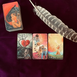 Peut inclure: Quatre cartes de tarot sur un fond de velours violet avec une plume sur le dessus. Les cartes sont "6 de Coupes", "Les Amoureux", "3 d'&Eacute;p&eacute;es" et "Le Soleil".