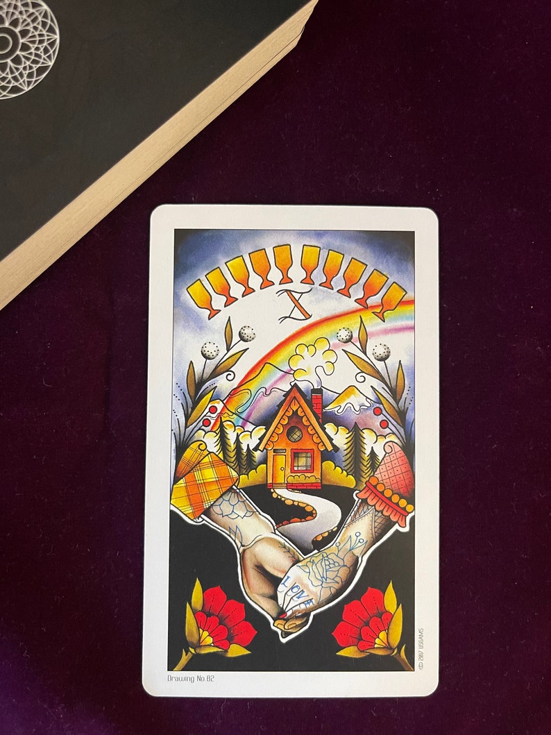 May include: Tarot card depicting the Ten of Cups, featuring a rainbow, a small house, and two hands holding each other. The hands are tattooed with hearts and the words "I love" and "you".