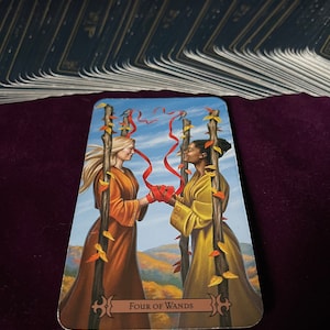 May include: Tarot card depicting the Four of Wands card. Two people are holding hands, standing in front of four wands with red ribbons tied around them. The background is a blue sky with white clouds and a landscape of green hills and trees. The card is titled "Four of Wands".