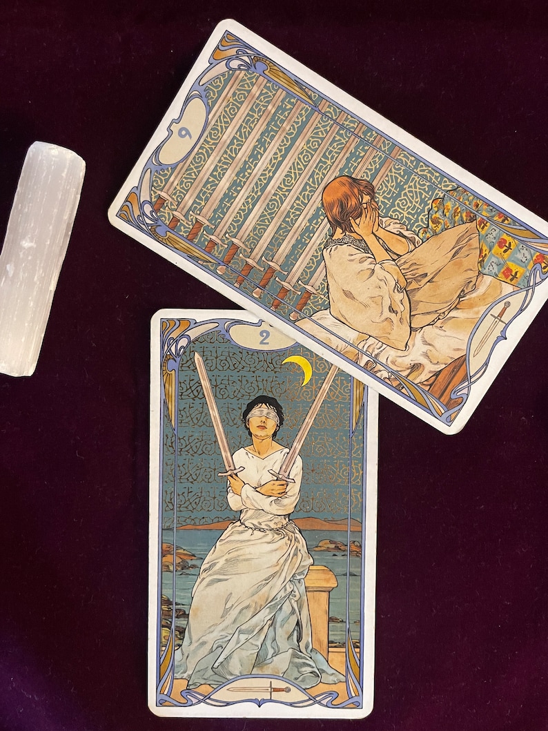 May include: Two tarot cards, the Nine of Swords and the Two of Swords. The Nine of Swords card depicts a woman with her head in her hands, surrounded by nine swords. The Two of Swords card shows a woman blindfolded, holding two swords crossed in front of her.