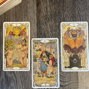 May include: Three tarot cards, the first card is the VI of Wands, the second card is the 6 of Cups, and the third card is the XV of the Devil. The cards are on a wooden surface.