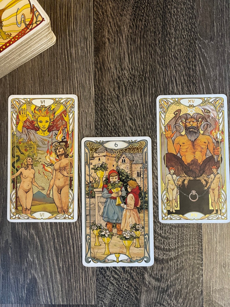 May include: Three tarot cards, the first card is the VI of Wands, the second card is the 6 of Cups, and the third card is the XV of the Devil. The cards are on a wooden surface.