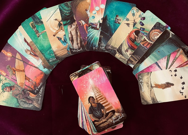 May include: A spread of tarot cards on a burgundy surface. The cards are arranged in a semi-circle with the "The Hierophant" card in the center. The cards feature colorful illustrations and text.