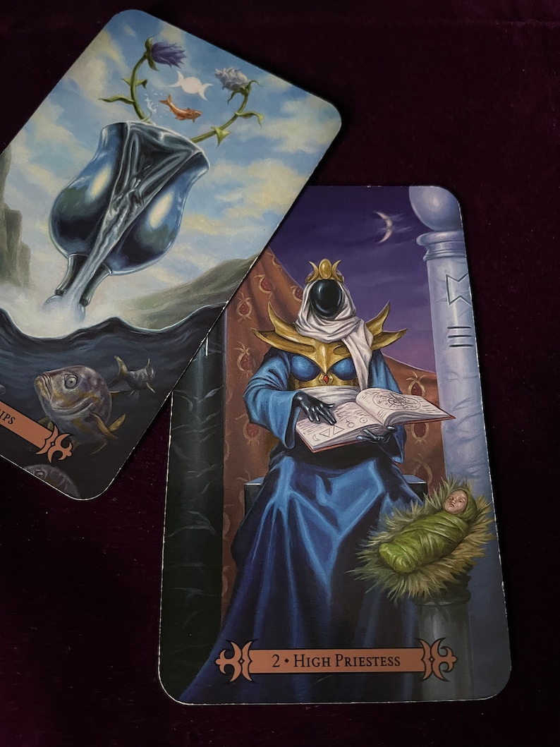 May include: Tarot card depicting the High Priestess, the second card in the Major Arcana. The card features a robed figure sitting on a throne, holding a book and a baby. The background is a dark blue with a crescent moon and stars.