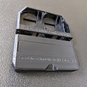May include: A black plastic 3D printed case with the text "nevermore micro v8" and "REPLACE CARBON EVERY 2-4 WEEKS" printed on it.