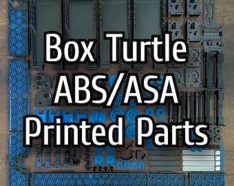 Op de afbeelding: Een verzameling zwarte en blauwe 3D-geprinte onderdelen, waaronder rechthoekige en geometrische vormen, gerangschikt op een houten oppervlak. De tekst "Box Turtle ABS/ASA Printed Parts" is over de afbeelding geplaatst.