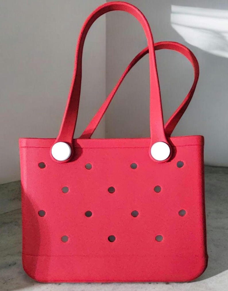 May include: A red tote bag with white handles and white buttons. The bag has a pattern of small holes.