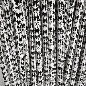 May include: A collection of white and black patterned straws. The straws are decorated with a repeating pattern of black bows. The straws are arranged closely together, creating a visually appealing display.