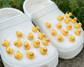 Könnte beinhalten: Weiße Clogs mit gelben Gummiente-Anhängern. Die Clogs sind ein beliebter Schuhstil.