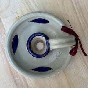 Puede incluir: Un portaincienso de cerámica hecho a mano, de color blanquecino con detalles azules. Tiene cortes en forma de hoja y un anillo azul. Una cinta burdeos está atada al asa.