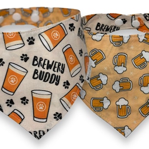 May include: Two dog bandanas with a beer theme. One bandana is white with orange beer mugs and paw prints, and the text "Brewery Buddy". The other bandana is orange with white beer mugs.