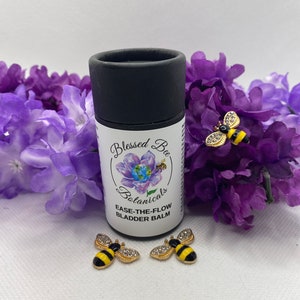 May include: A black tube with the text "Blessed Bee Botanicals Ease-The-Flow Bladder Balm" on a white label. The tube is surrounded by purple flowers and three gold bee charms with black and yellow stripes.