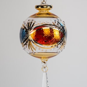 May include: A gold and clear glass Christmas bauble with a red and orange design and a crystal drop.