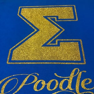 May include: A royal blue t-shirt with a gold glitter Greek letter Sigma and the word "Poodle" in gold glitter script.