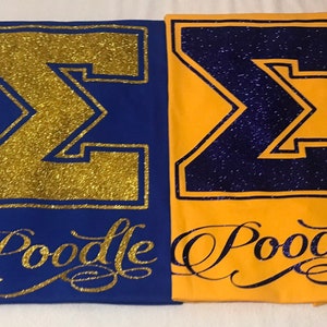 May include: Two t-shirts with a large gold glitter "&Sigma;" on a blue shirt and a large purple glitter "&Sigma;" on a yellow shirt. Both shirts have the word "Poodle" written in gold glitter below the letter.