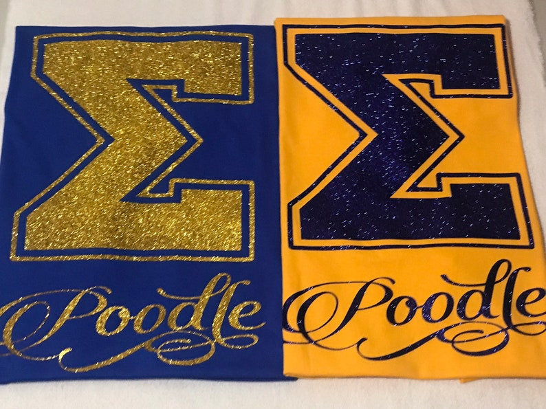 May include: Two t-shirts with a large gold glitter "&Sigma;" on a blue shirt and a large purple glitter "&Sigma;" on a yellow shirt. Both shirts have the word "Poodle" written in gold glitter below the letter.