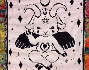 May include: A white crochet square with a black and white image of a goat with horns, wings, and a pentagram. The goat is sitting with its legs crossed and holding a heart in its hands. The background is filled with small white stars and diamonds.