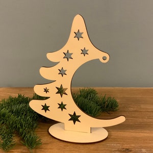 Puede incluir: Un adorno de árbol de Navidad de madera blanca con forma de media luna y estrellas recortadas. El adorno tiene una pequeña base.